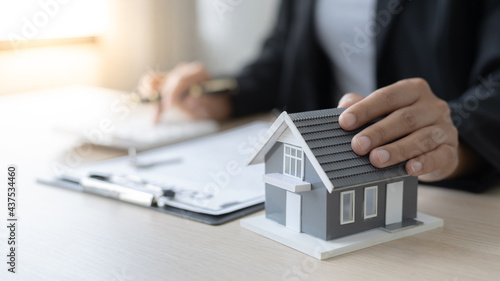 Selling a house with insurance, Salesperson or head of sales holds a model of the house with documentation and calculates the interest-tax-included payment to interested customers.