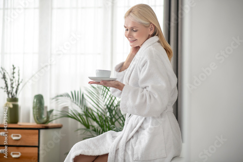 Woman in white robe having her morning coffee and looking pleased
