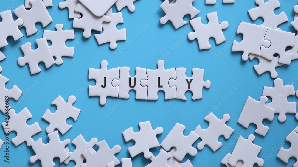 JULY word written on white jigsaw puzzle JULY word written on white jigsaw puzzle
