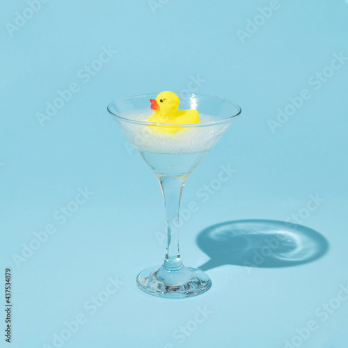 Obraz na plátně Creative composition with yellow rubber duck and bubble bath foam in martini cocktail glass on pastel blue background