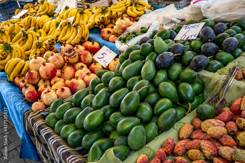 Heaps of avocados, pomegranates, bananas and prickly pear fruits on a table at a street farmers market in Alanya (Turkey). Outdoor sale of fruits and vegetables. Bright natural background