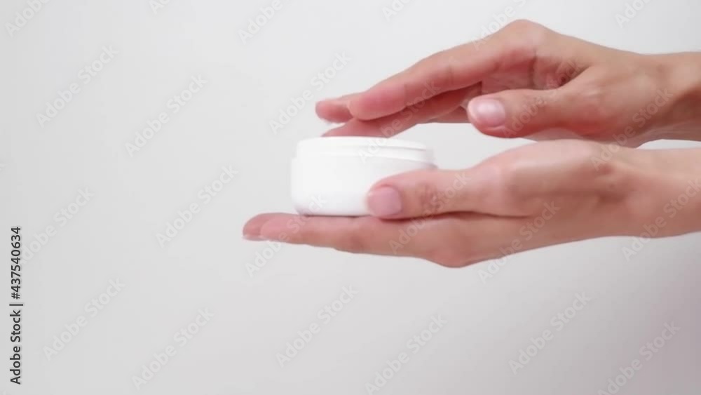 Woman's hands applying cream in a white jar, on a white background Woman's hands applying cream in a white jar, on a white background