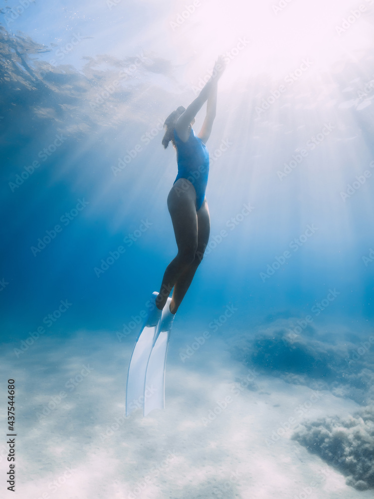 Naklejka premium Female freediver with fins glide underwater in sea with sunlight. Summer freediving.