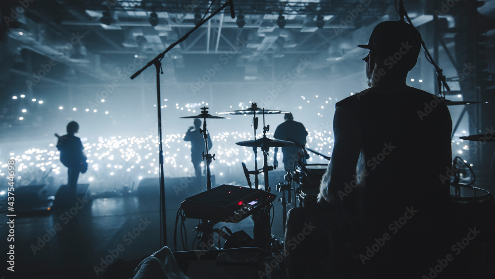© Таисия Овод - Music band group silhouette perform on a concert stage.  Silhouette of drummer playing on drumsaudience holding cigarette lighters and mobile phones