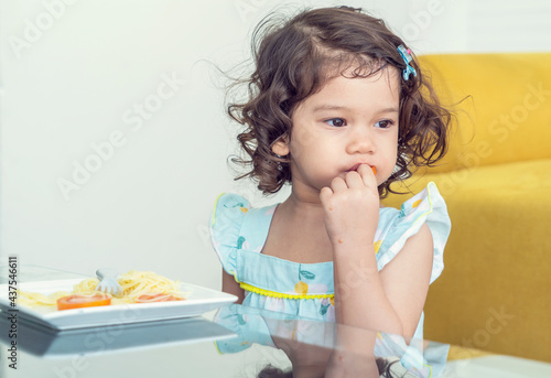 Canvastavla Hungry little girl eats delicious spaghetti in the house.