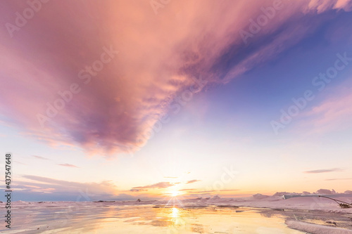 landscape pink clouds at dawn on cape khoboy olkhon island lake Baikal in winter on ice with cracked and large white bubbles
