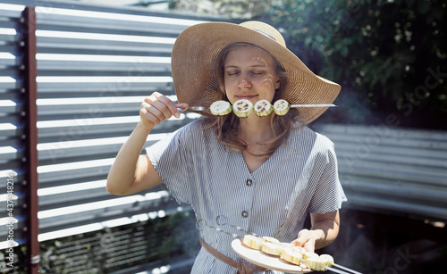 Young woman in summer hat smelling grilled vegetebles outdoors photo