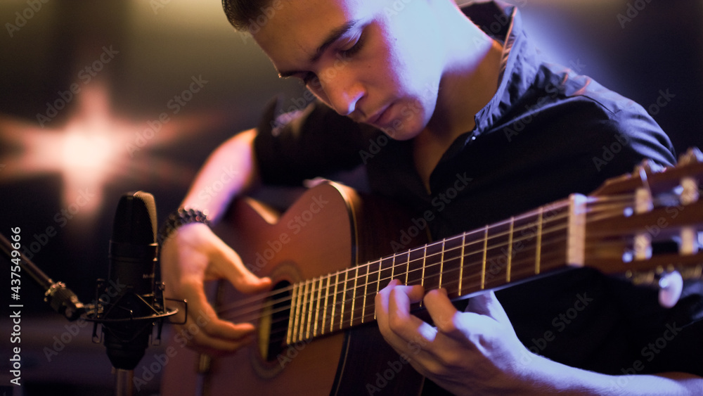 Obraz premium Man plays guitar. Young man plays a musical instrument. Musician records his composition in a music Studio using professional microphone