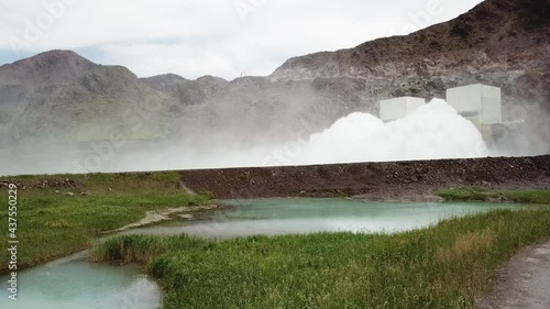 Dam with large discharge pressure of the water. Water dam. Shooting with the drone. Huge water pressure. Big fountain. Around the fountain grows grass, trees, running river. Summer nature. Small rocks photo