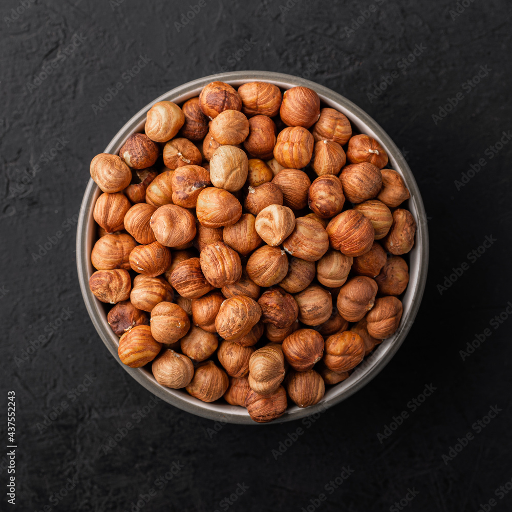 Peeled hazelnuts in a bowl on a black textured background, top view. Peeled hazelnuts in a bowl on a black textured background, top view.