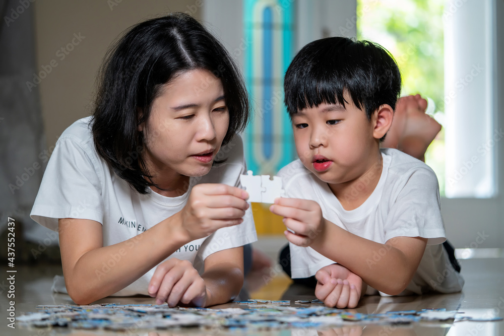 Asia family, Mother and son lying on the floor holding puzzle pieces and putting them together. Happy family during work at home. Woman teaches child to solve puzzles. Parent and cheerful concept. Asia family, Mother and son lying on the floor holding puzzle pieces and putting them together. Happy family during work at home. Woman teaches child to solve puzzles. Parent and cheerful concept.