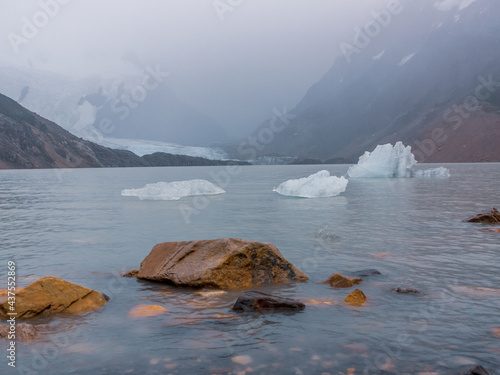 Andes, Patagagonia, Argentina. Los Glacieres National Park. Foggy Ladscape with Snowy Mountains.  Red Stones and Small Pieces of Glaciers in the Lake. Cloudy Sky.  photo