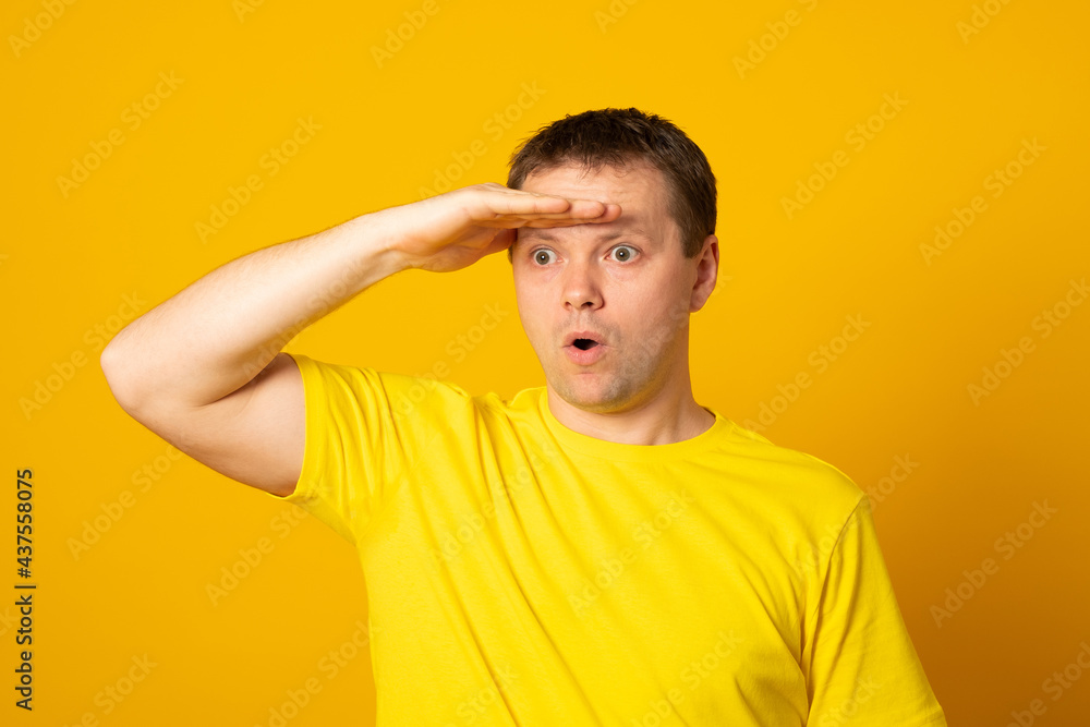 Young blond man wearing casual yellow shirt very happy and smiling looking far away with hand over head. Searching concept. Young blond man wearing casual yellow shirt very happy and smiling looking far away with hand over head. Searching concept.