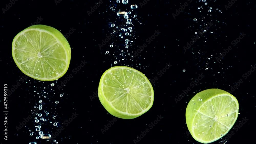 Limes splashing into the water in slow motion. Three half of limes falling slowly on a black background. Organic green citrus isolated on black background. Fresh water with fruits. Limes splashing into the water in slow motion. Three half of limes falling slowly on a black background. Organic green citrus isolated on black background. Fresh water with fruits.