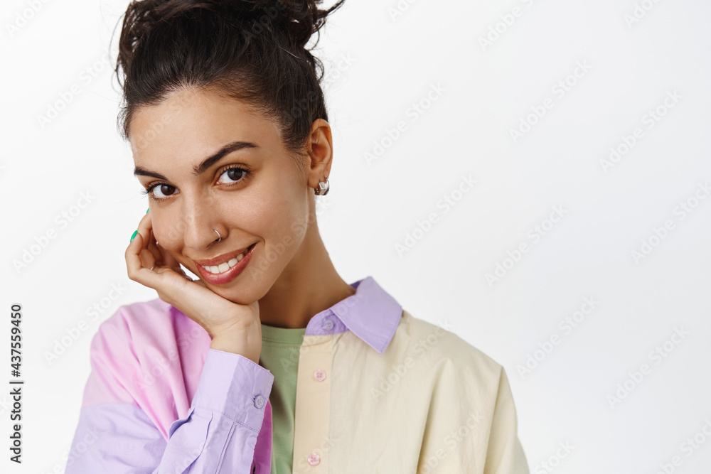 Skin care and cosmetology concept. Beautiful woman with dark curly hair, touch clean face and smiling white teeth, showing glowing natural facial skin, white background Skin care and cosmetology concept. Beautiful woman with dark curly hair, touch clean face and smiling white teeth, showing glowing natural facial skin, white background