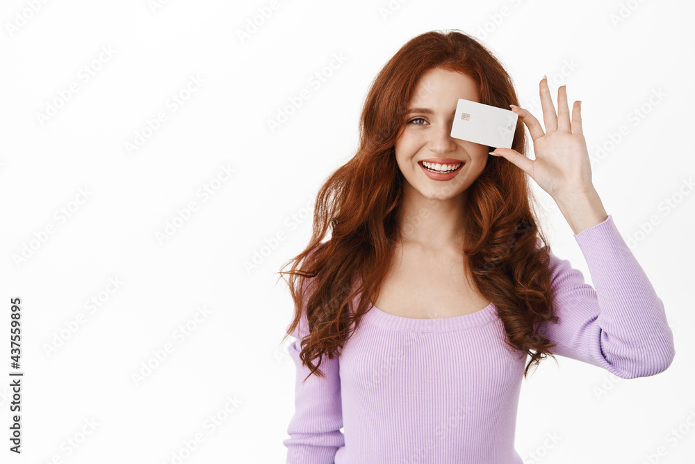 Portrait of beautiful redhead woman smiling white teeth, showing bank credit card, contactless payment, standing against white background Portrait of beautiful redhead woman smiling white teeth, showing bank credit card, contactless payment, standing against white background