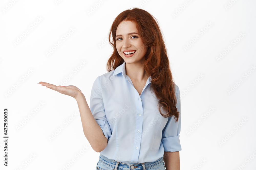 Modern young girl manager holding open hand, looking happy at camera, smiling demonstrating advertisement in palm, standing against white background Modern young girl manager holding open hand, looking happy at camera, smiling demonstrating advertisement in palm, standing against white background