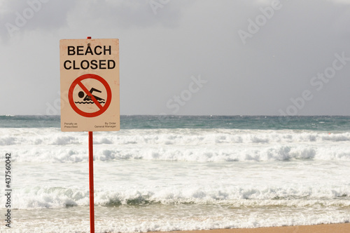 "Beach closed" sign with choppy seas in the background at Manly Beach, Sydney, Australia