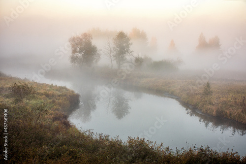 Autumn dense fog on the river, reflection of trees in the water © Alena