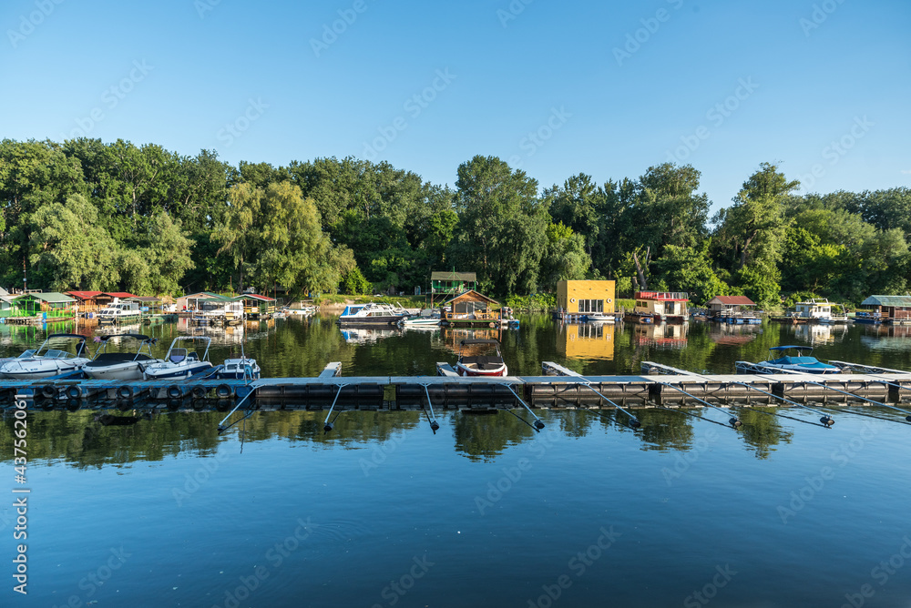 View of a floating summer houses intended for summer vacation with berths and a dock for boats and speedboats on the water surface of a river or lake