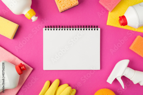 Top view photo of open planner scouring pads rags rubber gloves and white detergent bottles on isolated pink background with blank space