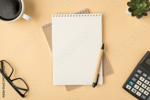 Top view photo of planners and pen in the middle cup of coffee flowerpot glasses calculator on isolated beige background with blank space