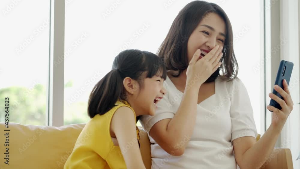 Asian mom and kid daughter laughing watching internet content on smartphone Asian mom and kid daughter laughing watching internet content on smartphone