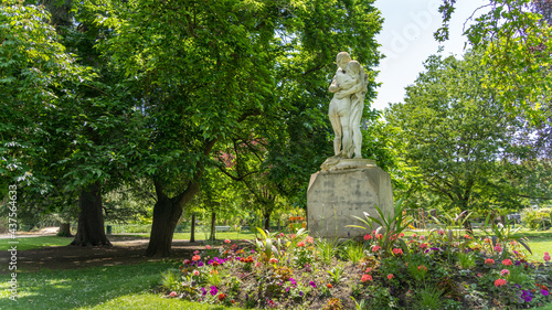 Pretty statues of a hugging couple, surrounded by trees and flowers