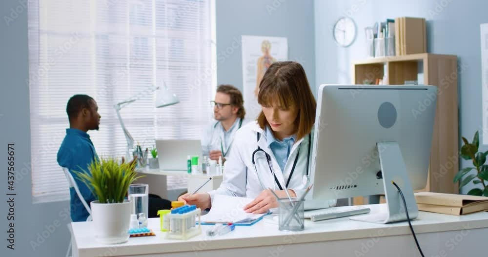 Beautiful caucasian female doctor sitting at table in office and filling out paper medical cards for patients. Beautiful caucasian female doctor sitting at table in office and filling out paper medical cards for patients.