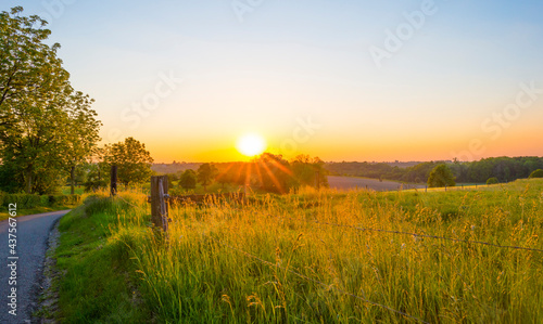 Sundown over fields and trees in a green hilly grassy landscape under a colorful sky in sunlight in springtime, Voeren, Limburg, Belgium, June, 2021