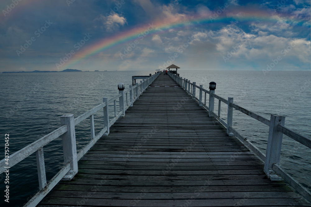 Wooden bridge in the sea, line leading the eye to the rainbow