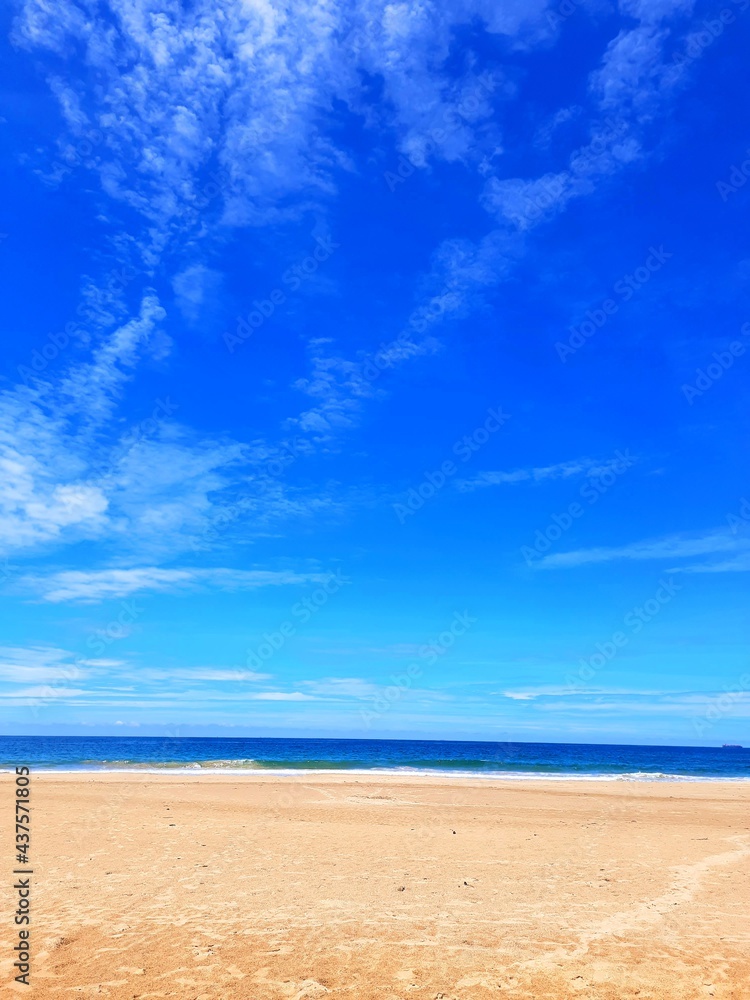 Krajobraz plaży z niebieskim niebem i chmurami oraz żółtym piaskiem. - obrazy, fototapety, plakaty 