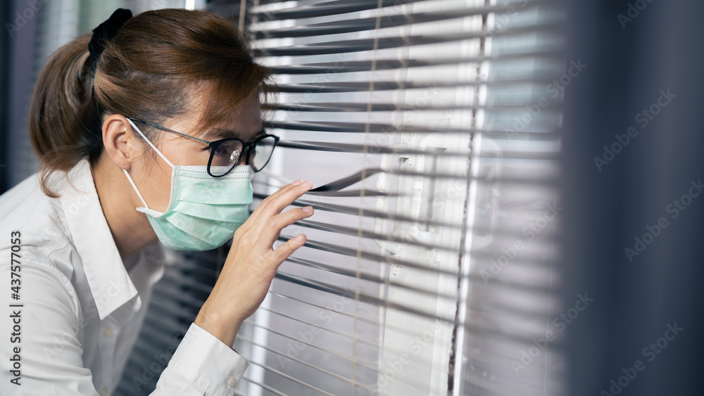 Business woman asian wearing mask while peeking something outside through curtain in office. Business woman asian wearing mask while peeking something outside through curtain in office.