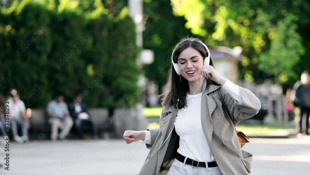 Young adult happy woman dancing in downtown very emotional. Slow motion of happy young woman in wireless headphones dancing singing outdoors in city street having fun alone Young adult happy woman dancing in downtown very emotional. Slow motion of happy young woman in wireless headphones dancing singing outdoors in city street having fun alone