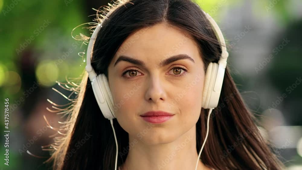Attractive Young Woman looks to the camera and smiles while listening to music wearing headphones outdoors Attractive Young Woman looks to the camera and smiles while listening to music wearing headphones outdoors
