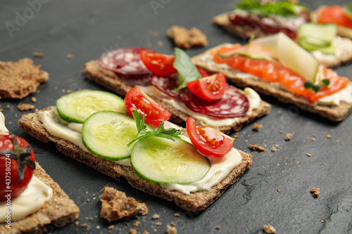 Fresh rye crispbreads with different toppings on black table, closeup