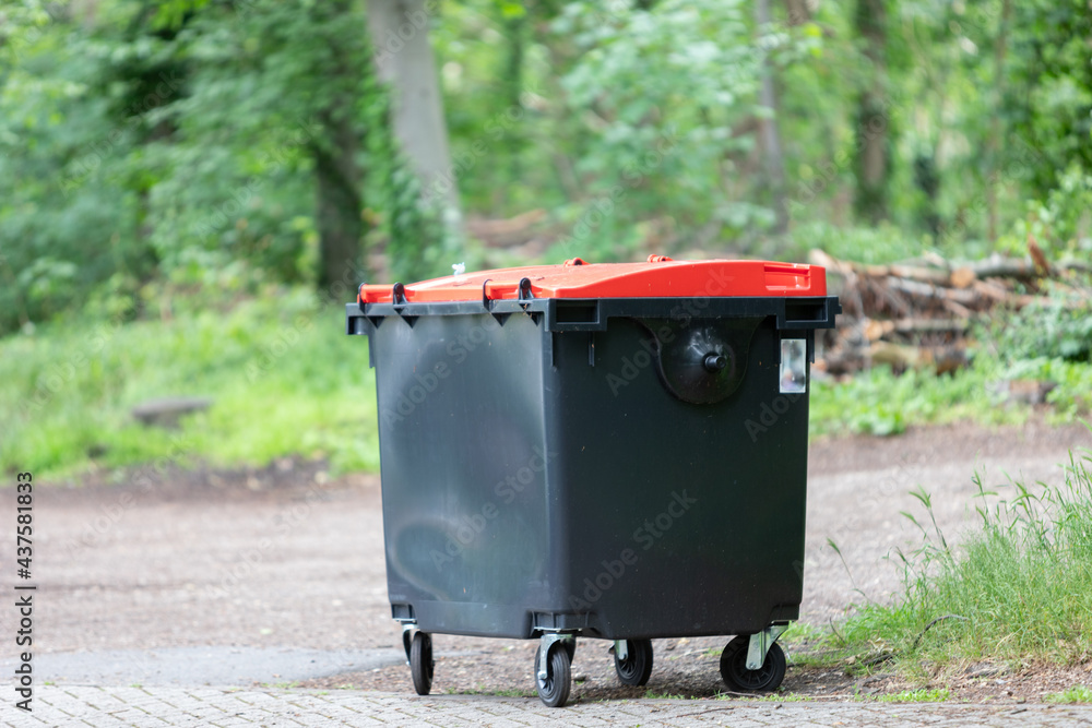 black garbage tin with red lid, forest in the background black garbage tin with red lid, forest in the background