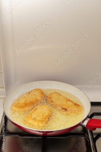 Pan with oil preparing fried bread with egg and flour (Torrijas). Typical Spanish Easter sweet. Traditional home cooking concept. Vertical photography and selective focus