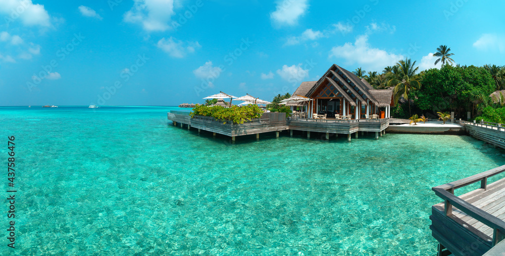 Amazing wide panorama of tropical Maldives island on a sunny day. Exotic vivid beach background with blue turquoise lagoon and palm trees. Luxurious holiday and romantic honeymoon destination.