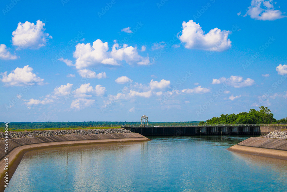 river dam water reservoir lake with surrounding walls and bright blue sunny sky and clouds reflection