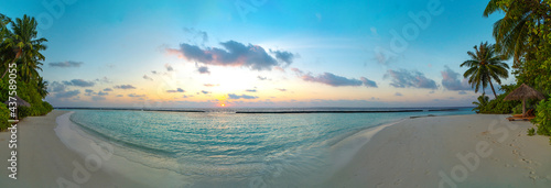 Amazing wide panorama of tropical Maldives island. Exotic beach background with blue lagoon, turquoise water and palm trees during beautiful sunrise. 