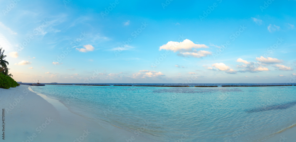 Fototapeta premium Amazing wide panorama of tropical Maldives island. Exotic beach background with blue lagoon, turquoise water and palm trees during beautiful sunrise. 