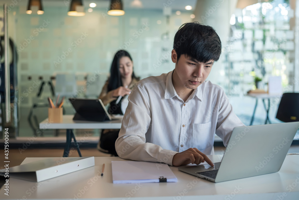 Front view of an Asian businessman sitting working on a laptop with blurry back. Front view of an Asian businessman sitting working on a laptop with blurry back.