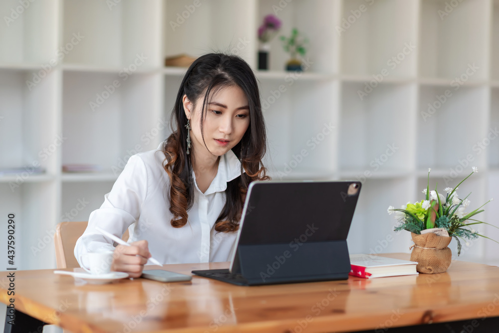 Asian businesswoman sitting at the office holding a pen smartphone and tablet placed on the table. Asian businesswoman sitting at the office holding a pen smartphone and tablet placed on the table.