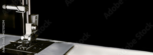 Metal needle of a white sewing machine close-up on a black background. Dark banner for sites about sewing production, needlework.
