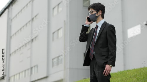 コロナ禍に屋外でビジネスパーソンがマスクをして電話をしながら咳込む1