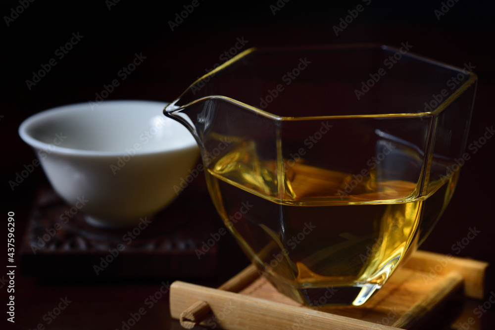 Still life of dishes for preparing a Chinese tea ceremony with a glass teapot, golden tea and a tea bowl against a dark background Still life of dishes for preparing a Chinese tea ceremony with a glass teapot, golden tea and a tea bowl against a dark background