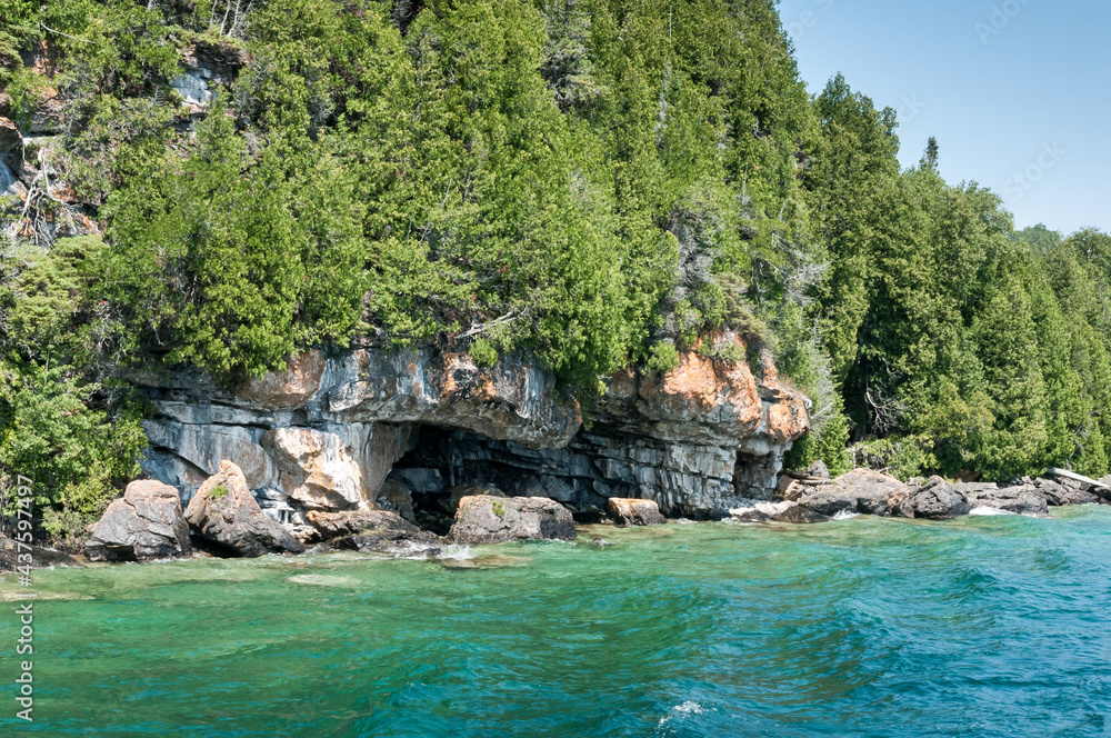 Trees with rocks on an island surrounded by blue, aqua, and clear water in Bruce Peninsula, Ontario, Canada.