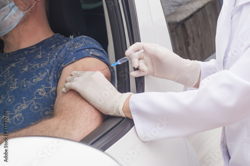 A nurse vaccinates a man who is sitting in a car.
