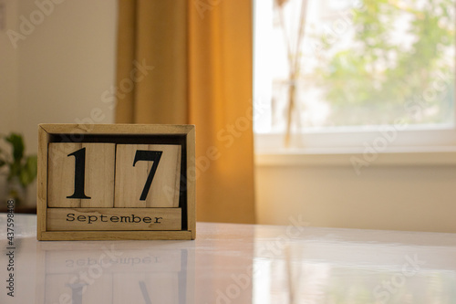 Wooden blocks of the calendar represents the date 17 and the month of September on the background of a window, curtain and a plant.